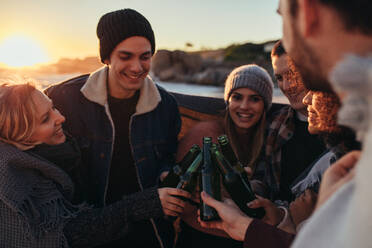 Eine Gruppe multiethnischer junger Leute stößt am Strand mit einem Bier an. Freunde verbringen ihre Zeit am Strand mit ein paar Drinks bei Sonnenuntergang. - JLPSF15944