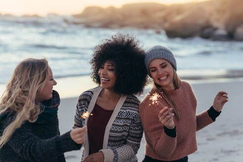 Glückliche Freunde feiern am Strand mit Wunderkerzen. Verschiedene Gruppe von Frauen Freunde zusammen am Strand feiern Neujahrstag am Strand. - JLPSF15954