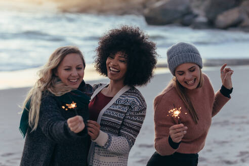 Eine Gruppe von Freundinnen hat Spaß mit Wunderkerzen am Strand. Eine Gruppe junger Frauen feiert den Neujahrstag am Strand. - JLPSF15955