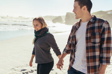 Verliebtes Paar, das am Strand spazieren geht. Junger Mann und Frau halten sich an den Händen und spazieren am Meer. - JLPSF15962