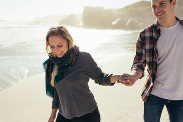 Outdoor shot of happy young couple walking on the beach holding hands. Young woman enjoying beach holidays with boyfriend. - JLPSF15963