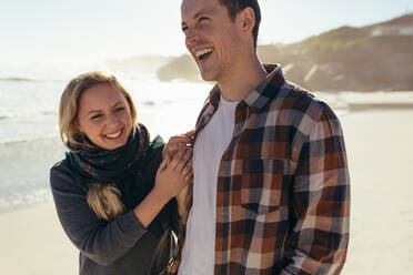 Gut aussehender Mann, der mit seiner Freundin am Strand spazieren geht. Fröhliches junges Paar, das gemeinsam am Meer entlang spaziert. - JLPSF15966