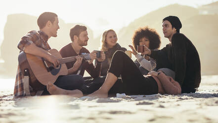 Junger Mann spielt Gitarre für Freunde am Strand. Eine Gruppe von Freunden feiert eine Party am Meer. - JLPSF15968