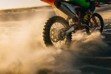 Rückansicht eines Motorradfahrers, der beim Motocross auf einer Sandbahn fährt, auf der Schmutz herumfliegt. - JLPSF15978