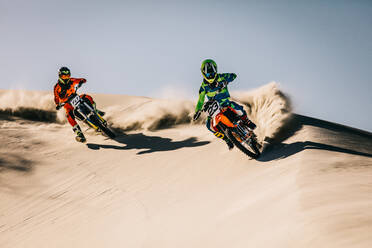 Two motocross racers speeding along the sand dunes. Dirt bikers in action in desert. - JLPSF15982