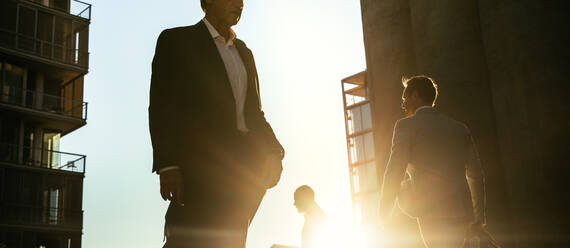 Männer in formeller Kleidung auf dem Weg ins Büro am frühen Morgen mit Bürotaschen. Geschäftsleute in Eile zu erreichen Büro zu Fuß auf der Straße der Stadt mit Sonne Flare im Hintergrund. - JLPSF15984