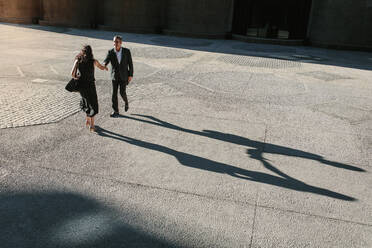 Eine Geschäftsfrau und ein Geschäftsmann, die sich auf der Straße die Hände schütteln, mit ihren langen Schatten auf dem Boden. Geschäftsleute, die sich auf dem Weg ins Büro auf der Straße begrüßen und die Hände schütteln. - JLPSF15990