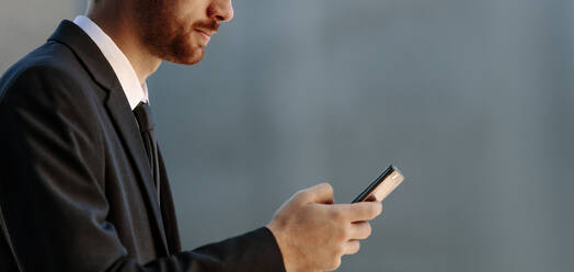 Close up shot of a man using his mobile phone. Businessman in formal clothes looking at his mobile phone. - JLPSF15996