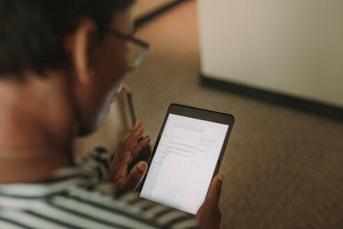 Frau in einem Hotelzimmer, die mit einem digitalen Tablet ihre E-Mails abruft; Fokus auf den Tablet-Computer in der Hand der Geschäftsfrau. - JLPSF16001