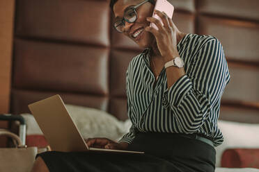 Happy Business-Frau mit Laptop und sprechen auf dem Handy, während auf dem Hotelzimmer Bett sitzen. Frau CEO auf Geschäftsreise arbeiten von Hotelzimmer. - JLPSF16002