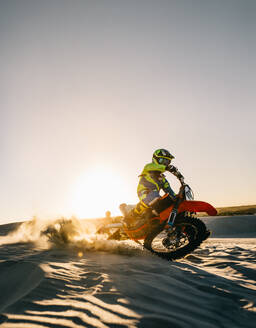 Motocross-Rennfahrer, der sein Motorrad auf Sanddünen dreht, wobei der Dreck nach hinten fliegt. Dirt-Biker, der in extremem Gelände fährt. - JLPSF16017