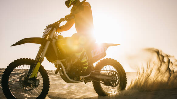 Motocross-Fahrer, der schnell auf Sanddünen fährt, wobei Schmutz herumfliegt. - JLPSF16025