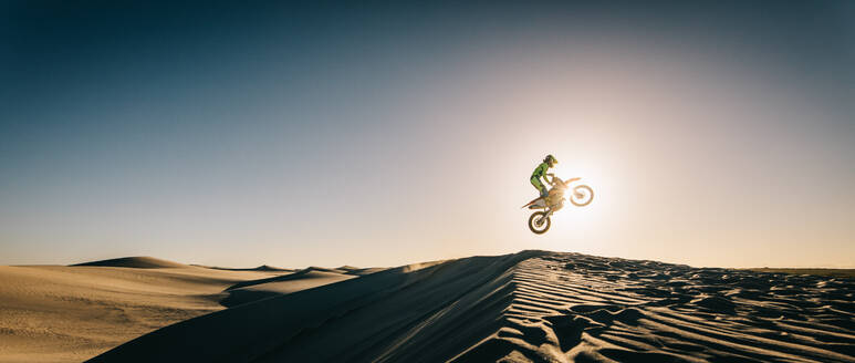 Motocross-Fahrer in der Luft während einer Fahrt. Seitenansicht eines Motorradfahrers, der über eine Sanddüne springt. - JLPSF16028