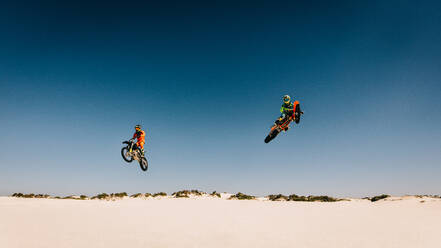 Motocross racers jumping bikes and doing stunts in desert. Dirt biker in mid air performing stunts. - JLPSF16039