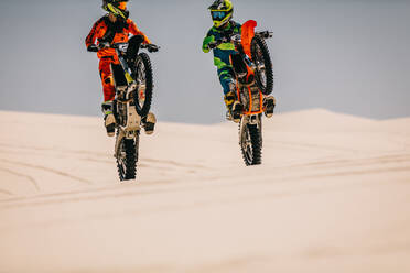 Zwei Motocross-Fahrer vollführen einen synchronen Wheelie in der Wüste. Stuntbiker zeigen ihr Können. - JLPSF16043