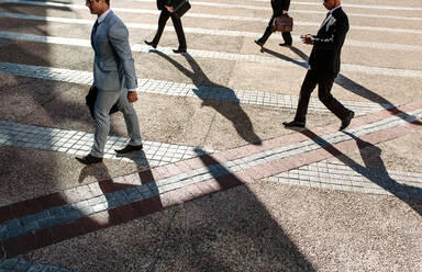 Männer auf dem morgendlichen Weg ins Büro, die ihre Bürotaschen tragen. Geschäftsleute, die es eilig haben, ihr Büro zu erreichen, gehen auf der Straße spazieren, wobei einige ihr Mobiltelefon benutzen. - JLPSF16093