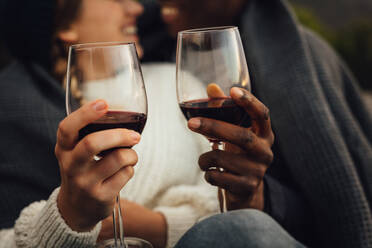 Ausschnitt eines Mannes und einer Frau, die bei einem Picknick mit Wein anstoßen. Ein Paar genießt ein Picknick im Freien mit Wein an einem kalten Wintertag. - JLPSF16102