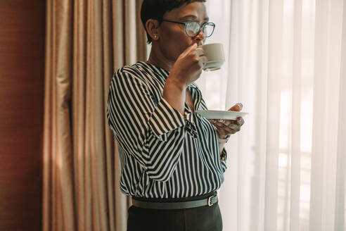 Mature female in formal clothes having coffee in hotel room. Businesswoman on business trip drinking coffee in hotel room. - JLPSF16132