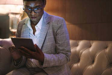 Reife afrikanische Frau in formeller Kleidung, die an der Hotelrezeption sitzt und ein digitales Tablet benutzt. Weiblicher CEO auf Geschäftsreise, der einen Tablet-PC in der Hotellobby benutzt. - JLPSF16146