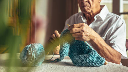 Close up of old man hands knitting with needles and wool yarn. Retired man knitting at home. - JLPSF16169