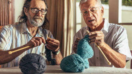 Zwei ältere Freunde stricken zu Hause. Ältere Männer fertigen mit Nadeln und Wollgarn warme Kleidung an. - JLPSF16173