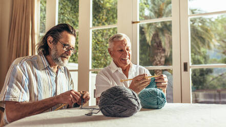 Alte Männer, die zu Hause sitzen und mit Stricknadeln und Wollfäden Pullover stricken. Ältere Menschen, die im Ruhestand stricken lernen. - JLPSF16175