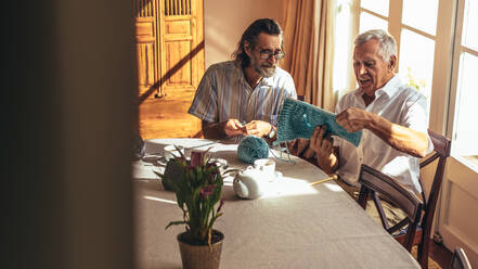Zwei Männer im Ruhestand sitzen am Tisch und stricken zu Hause. Ältere Freunde fertigen Wollkleidung mit Nadeln und Wollgarn an. - JLPSF16180