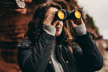 Young woman in nature and enjoying view using binoculars. Woman traveler looking through binoculars. - JLPSF16237