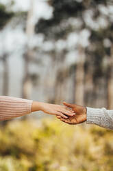 Interracial couple hands reaching to each other outdoors. Couple approaching to each other and holding hands. - JLPSF16257