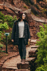 Touristin, die auf einer Steinböschung am Berg steht und wegschaut. Frau in warmer Kleidung im Winterurlaub. - JLPSF16278