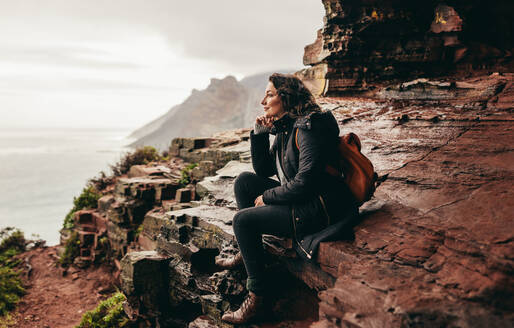 Frau sitzt auf einem Berg und genießt die Aussicht, eine Reisende entspannt sich auf einem felsigen Berg. - JLPSF16283