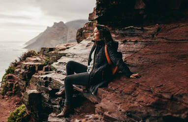 Weibliche Touristin, die sich auf einem felsigen Berg ausruht und die schöne Aussicht bewundert. Schöne Frau, die sich auf einem Berggipfel ausruht und die Aussicht betrachtet. - JLPSF16284