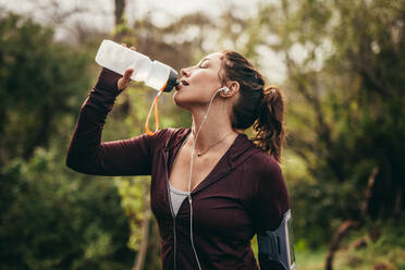 Eine Läuferin trinkt Wasser nach einem Lauftraining im Freien. Eine Frau trinkt nach einem Lauftraining Wasser. - JLPSF16290