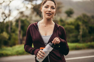 Porträt einer schönen Fitness-Frau mit Wasserflasche, die in die Kamera schaut. Eine Läuferin macht eine Pause nach dem Training am Morgen. - JLPSF16292