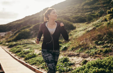 Woman running outdoors and looking at the view. Female doing jogging exercise on path by the mountain. - JLPSF16294