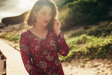 Porträt einer hübschen jungen Frau im roten Kleid, die im Freien steht. Weibliches Modell, das an einem sonnigen Tag im Freien posiert. - JLPSF16297