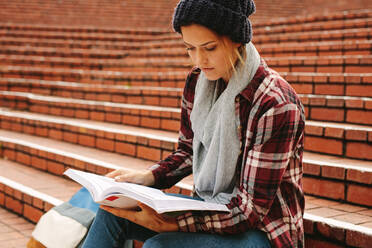 Junge Frau, die auf einer Universitätstreppe ein Buch liest. Kaukasische Studentin, die sich auf Prüfungen am College vorbereitet. - JLPSF16300