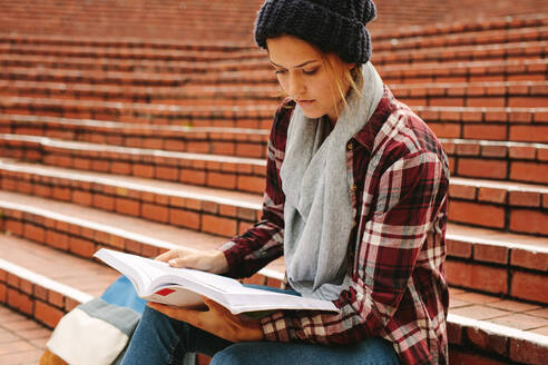 Junge Frau, die auf einer Universitätstreppe ein Buch liest. Kaukasische Studentin, die sich auf Prüfungen am College vorbereitet. - JLPSF16300