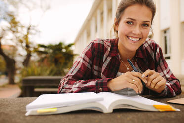 Smiling female student sitting at college campus with books. Girl student studying at university campus. - JLPSF16307