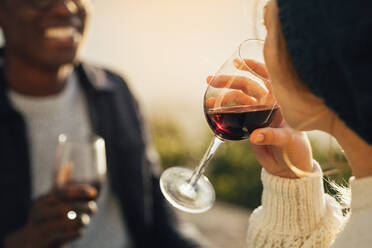 Nahaufnahme einer Frau beim Weintrinken mit ihrem Freund, der hinten sitzt. Ein Paar beim Picknick mit Fokus auf das Weinglas in der Hand der Frau. - JLPSF16346