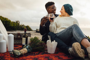 Mann und Frau stoßen beim Picknick mit Weingläsern an. Ein Paar trinkt Wein bei einem romantischen Date im Freien. - JLPSF16349