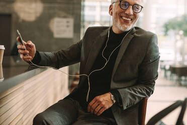 Handsome reifen Mann sitzt im Café hören Musik für Handy. Business-Mann sitzt vor Café Zähler genießen Musik über Kopfhörer von Smartphone zu hören. - JLPSF16360