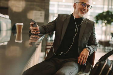 Happy reifen Geschäftsmann sitzt im Café hören Musik für Handy. Geschäftsmann sitzt vor Café Zähler genießen Musik hören über Kopfhörer von Handy. - JLPSF16361