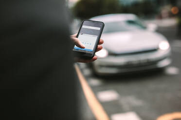 Mann bittet um Abholung durch ein Taxi über sein Telefon via Ride-Sharing-Anwendung. Fokus auf Mann Hand hält Telefon mit einem Auto im Hintergrund. - JLPSF16385