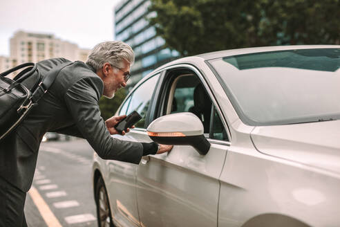 Ein älterer Mann steht auf der Straße und unterhält sich durch ein geöffnetes Autofenster mit einem Taxifahrer, der ein Taxi nimmt, um zu reisen. - JLPSF16390