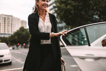 Lächelnde Pendlerin beim Aussteigen aus einem Taxi. Geschäftsfrau beim Aussteigen aus einem Taxi. - JLPSF16399