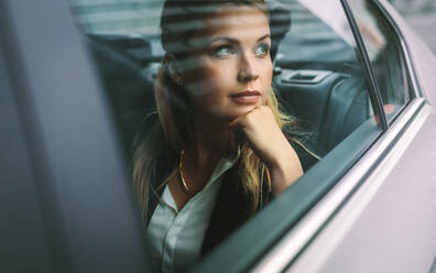 Beautiful young businesswoman sitting on back seat of a car and looking outside the window. Female business executive travelling by a cab. - JLPSF16402