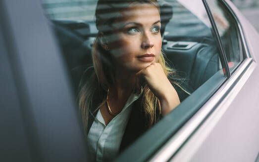 Schöne junge Geschäftsfrau, die auf dem Rücksitz eines Autos sitzt und aus dem Fenster schaut. Weibliche Geschäftsfrau, die mit einem Taxi unterwegs ist. - JLPSF16402