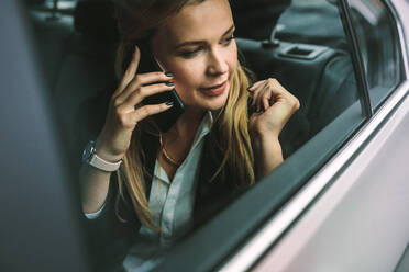 Junge Geschäftsfrau, die auf dem Rücksitz eines Autos sitzt und mit dem Handy telefoniert. Kaukasische weibliche Führungskraft, die in einem Taxi reist und mit dem Handy telefoniert. - JLPSF16403