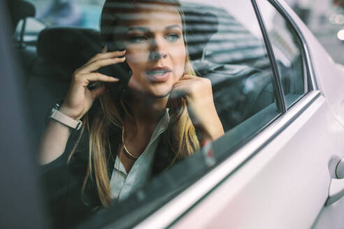 Schöne junge Geschäftsfrau, die auf dem Rücksitz eines Autos sitzt und telefoniert. Weibliche Führungskraft, die mit einem Taxi ins Büro fährt. - JLPSF16404
